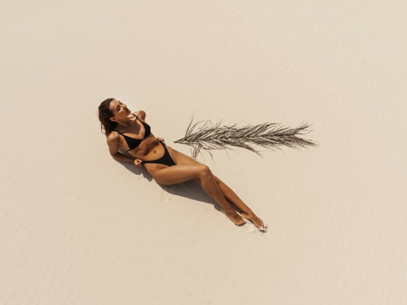 gommage et bronzage : femme qui bronze sur une plage de sable