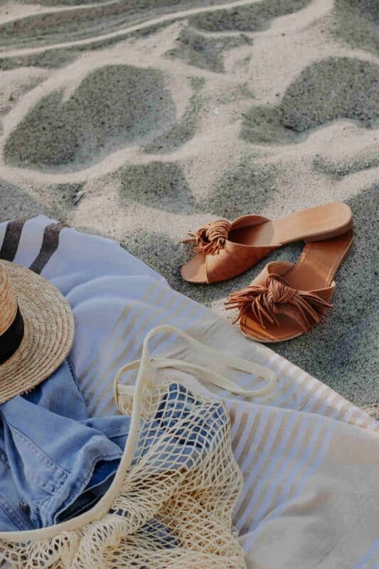 combien de temps pour bronzer : serviette de plage, claquettes et chapeau sur le sable