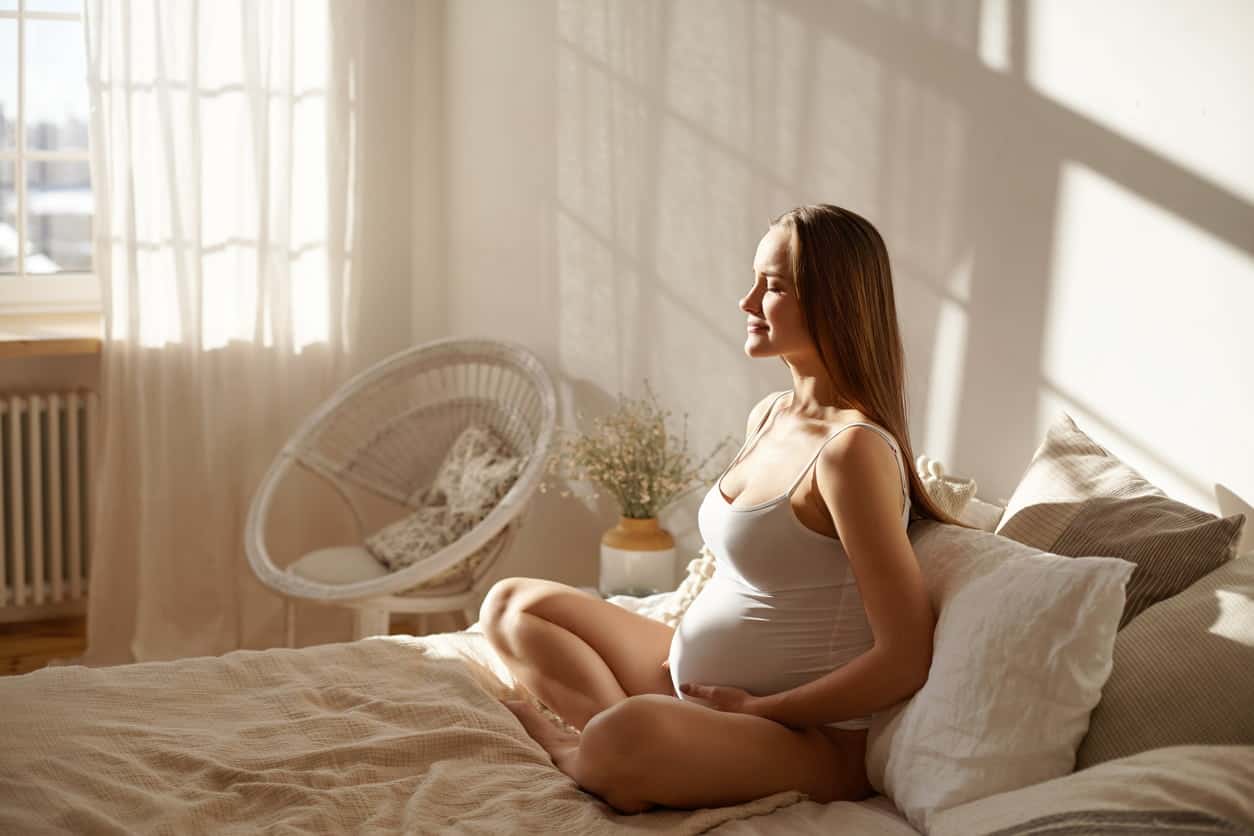 comment bien dormir enceinte : femme sur son lit en train de faire de la méditation