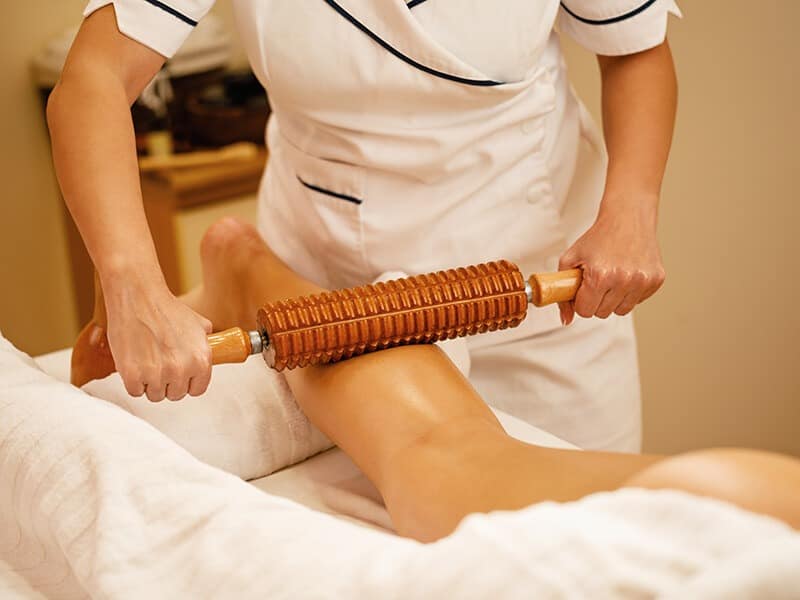 massage maderotherapie : une personne se fait masser les jambes avec un outil en bois